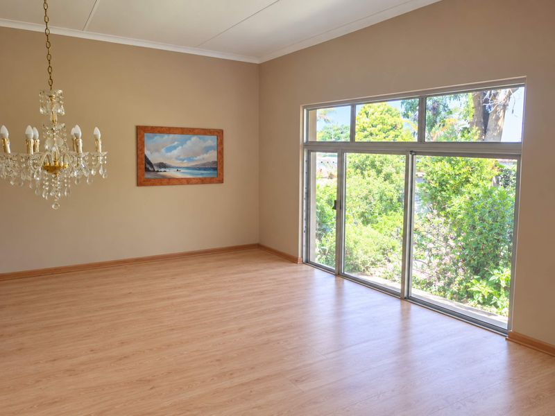 Spacious living area featuring light wood-look laminate flooring, a classic crystal chandelier, and large sliding glass doors providing ample natural light and garden views.
