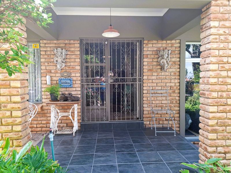 A covered entrance patio featuring exposed brick pillars, dark tiled flooring, and a decorative security gate.