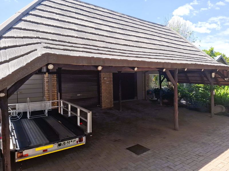 A covered carport area featuring a tiled roof, timber support posts, and brick pillars, providing sheltered parking with roller shutter garage access.