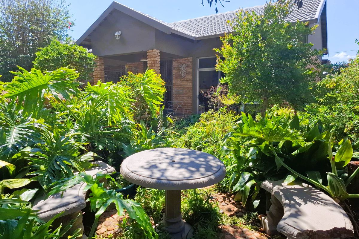 A view of the rear exterior of the house featuring a covered patio with brick pillars and a lush, established garden.