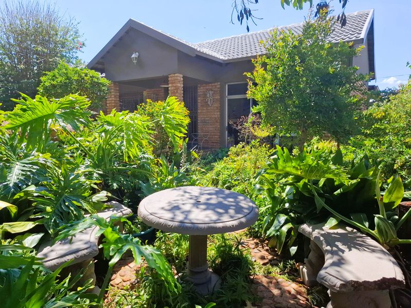 A view of the rear exterior of the house featuring a covered patio with brick pillars and a lush, established garden.