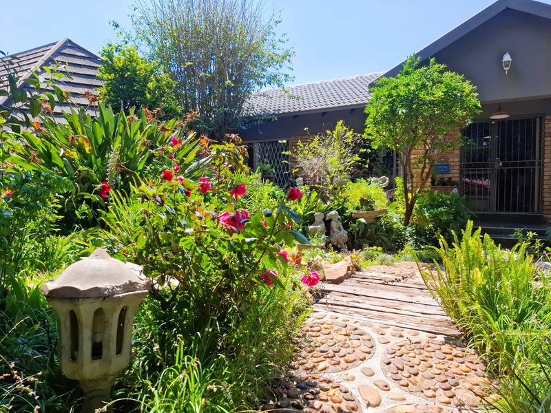A lush, well-established garden featuring a stone pathway leading toward the house entrance, complemented by mature greenery and a tiled roof structure.