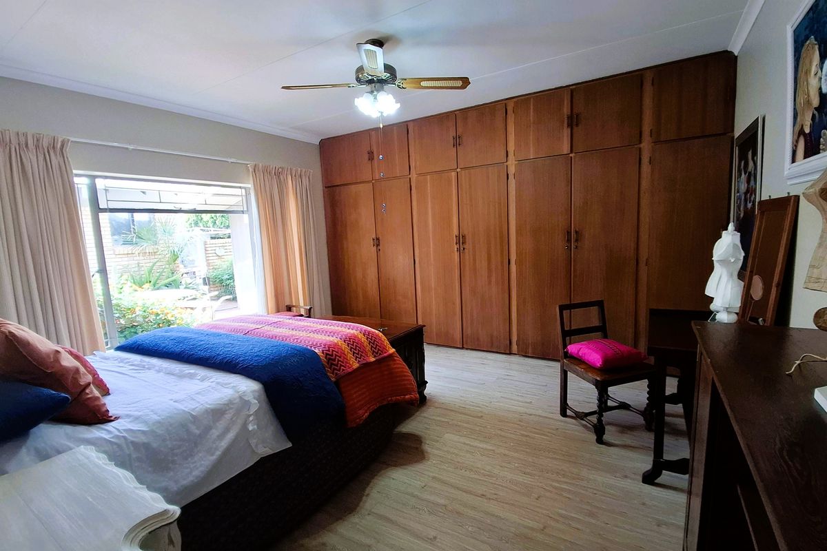 Spacious bedroom featuring extensive built-in wooden cabinetry, laminate flooring, and a sliding door providing direct access to the garden area.