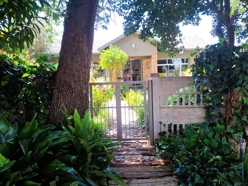A charming front entrance featuring a brick boundary wall, metal pedestrian gate, and a paved walkway leading to the main house facade.