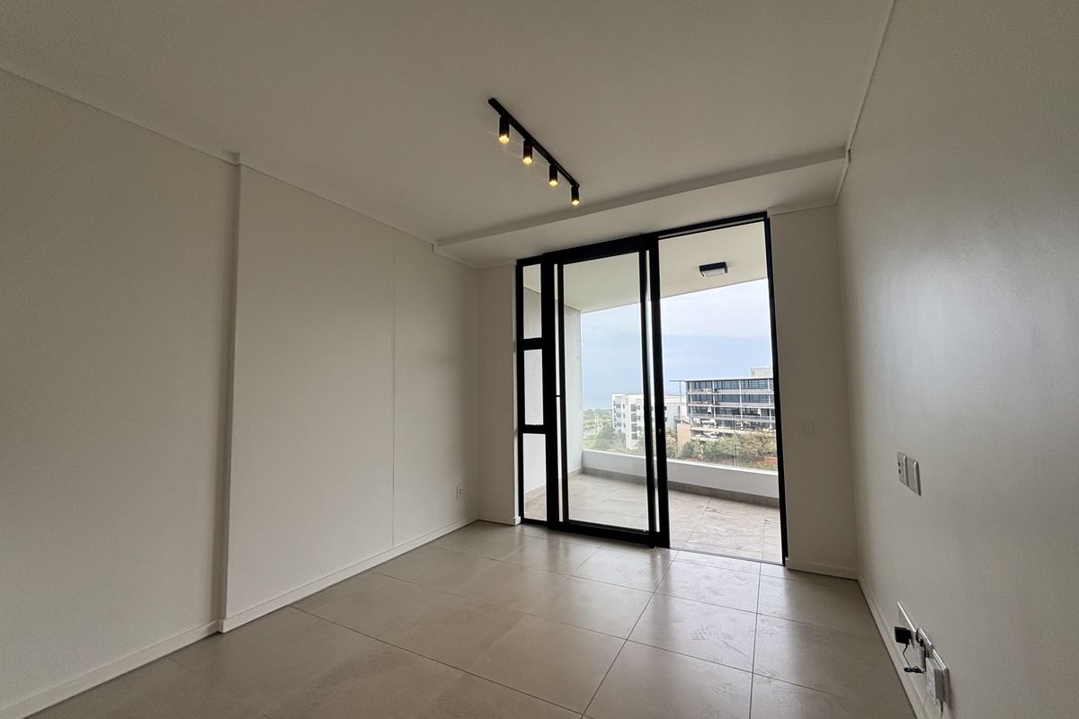 A bright, empty bedroom featuring modern tiled flooring, track lighting, and a sliding glass door providing direct access to a private balcony.