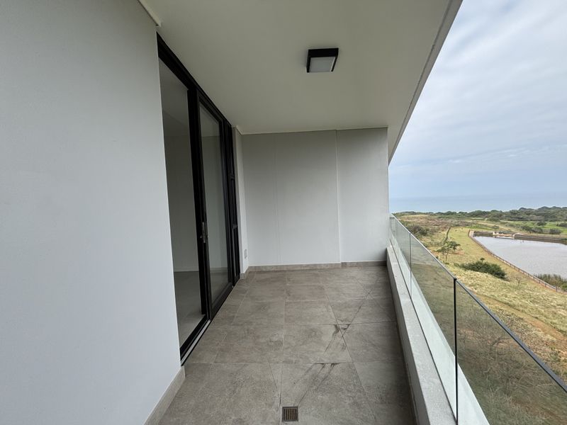 A modern, covered balcony featuring tiled flooring, a sleek glass balustrade, and expansive views of the surrounding landscape and coastline.