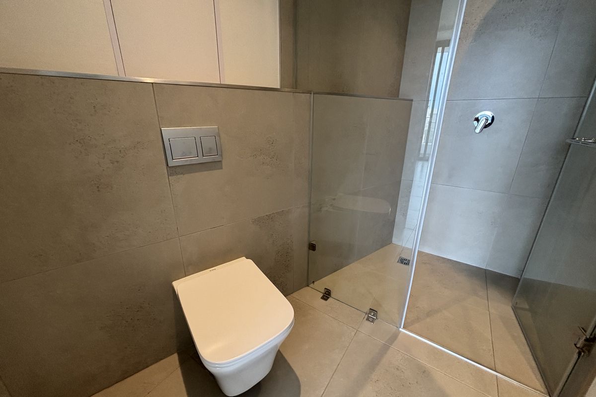 Modern bathroom featuring a wall-hung toilet with concealed cistern and a walk-in shower with a glass screen and neutral tiling.