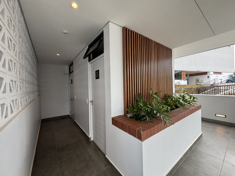 A modern, well-maintained hallway featuring a decorative timber slat wall, built-in brick planter, and stylish breeze block detailing.