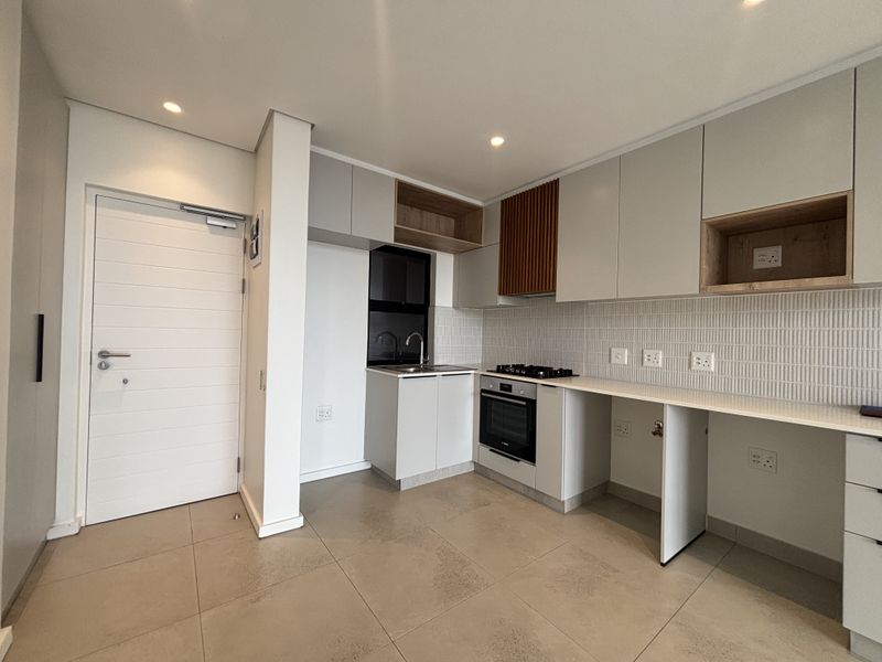 Modern kitchen featuring sleek built-in cabinetry, stone countertops, gas hob, built-in oven, and contemporary tiled backsplash in a clean, open-plan layout.