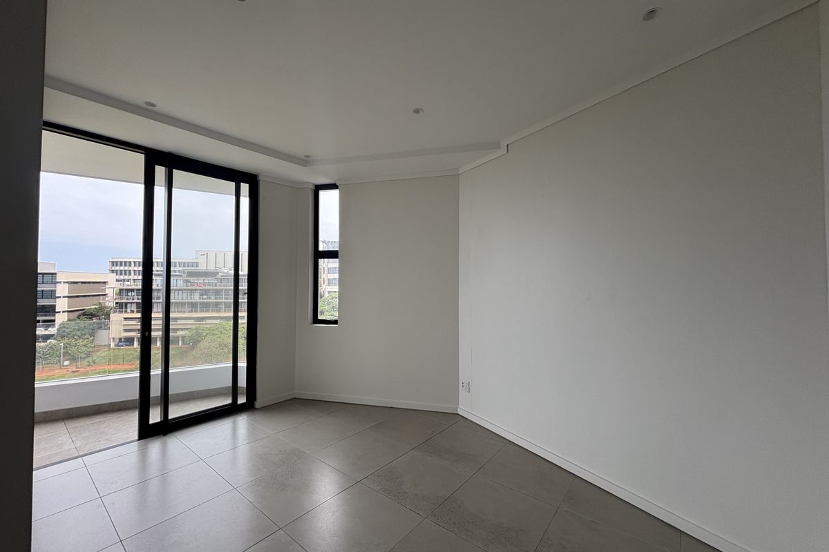 A bright, modern, and empty living area featuring large windows, sliding glass doors leading to a balcony, and neutral tiled flooring.