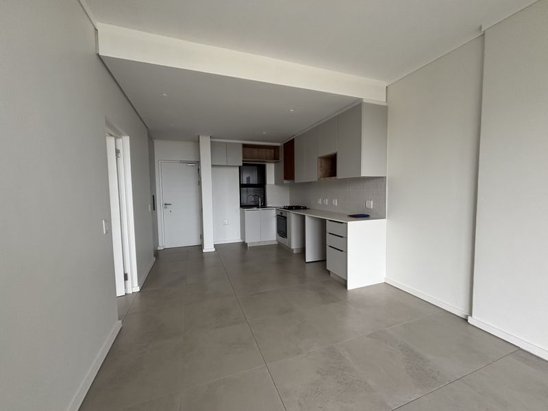 Modern open-plan kitchen and living area featuring neutral tiled flooring, sleek built-in cabinetry, and integrated appliances in a clean, minimalist space.