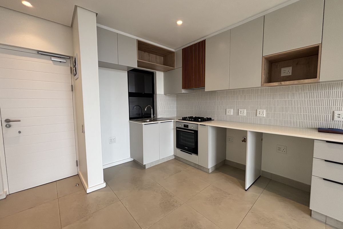 Modern kitchen featuring sleek cabinetry, built-in gas hob and oven, tiled backsplash, and neutral floor tiles in a clean, contemporary apartment setting.