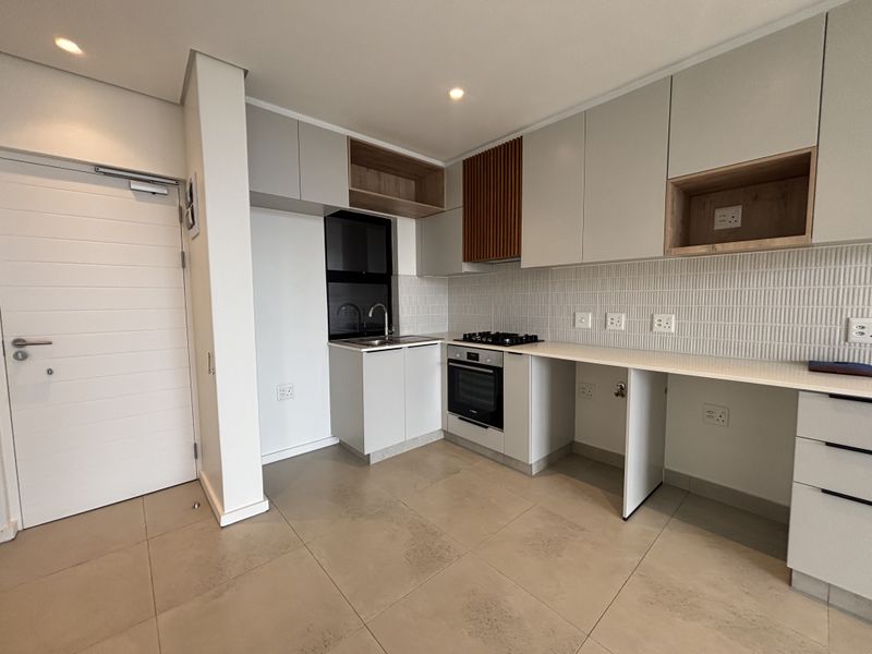 Modern kitchen featuring sleek cabinetry, built-in gas hob and oven, tiled backsplash, and neutral floor tiles in a clean, contemporary apartment setting.