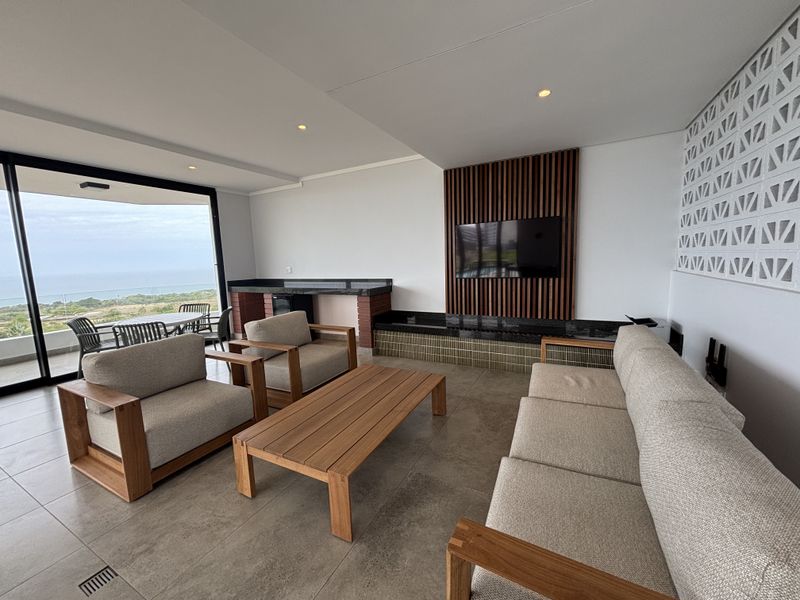 Spacious covered balcony featuring a built-in bar, timber slat feature wall, and sliding glass doors offering expansive coastal views.