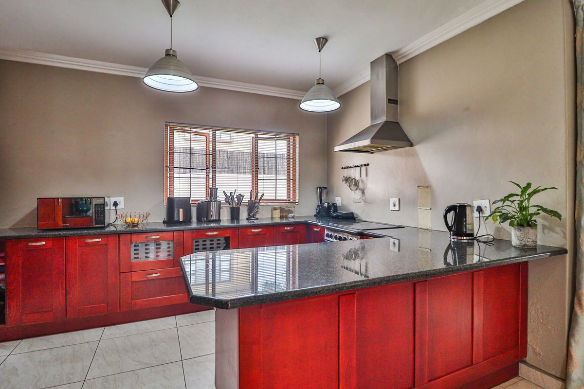 A functional kitchen featuring dark wood cabinetry, granite countertops, a stainless steel extractor fan, and tiled flooring.