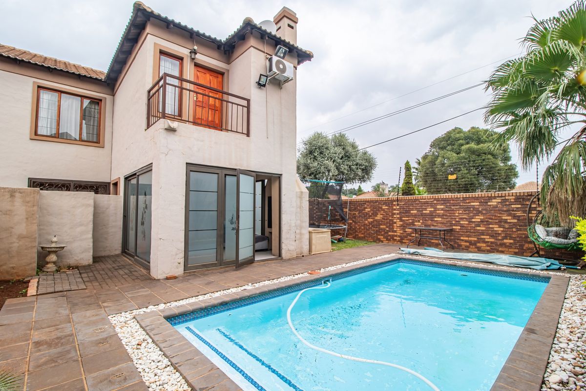 Rear exterior view featuring a swimming pool, paved patio area, and a two-story building structure with a balcony and sliding glass doors.