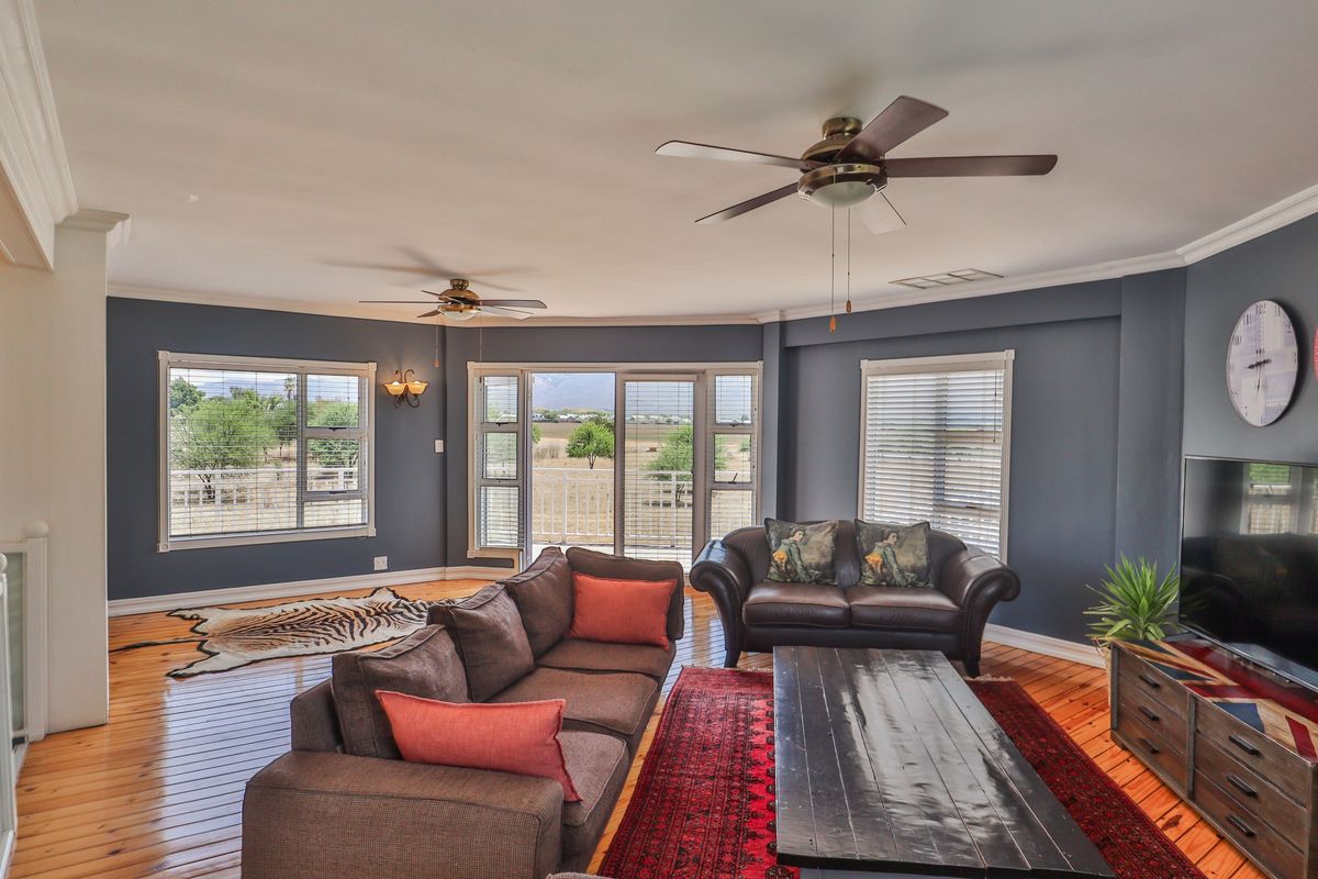 Spacious living room featuring hardwood flooring, crown molding, dual ceiling fans, and large windows with sliding glass doors leading to an outdoor area.
