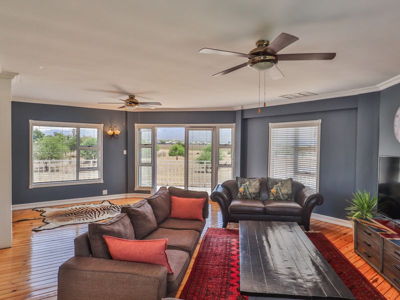 Spacious living room featuring hardwood flooring, crown molding, dual ceiling fans, and large windows with sliding glass doors leading to an outdoor area.