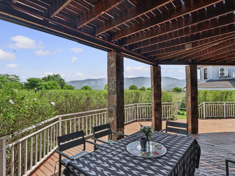 Spacious covered patio featuring timber decking, stone-clad columns, and a timber pergola, offering scenic mountain views and direct garden access.