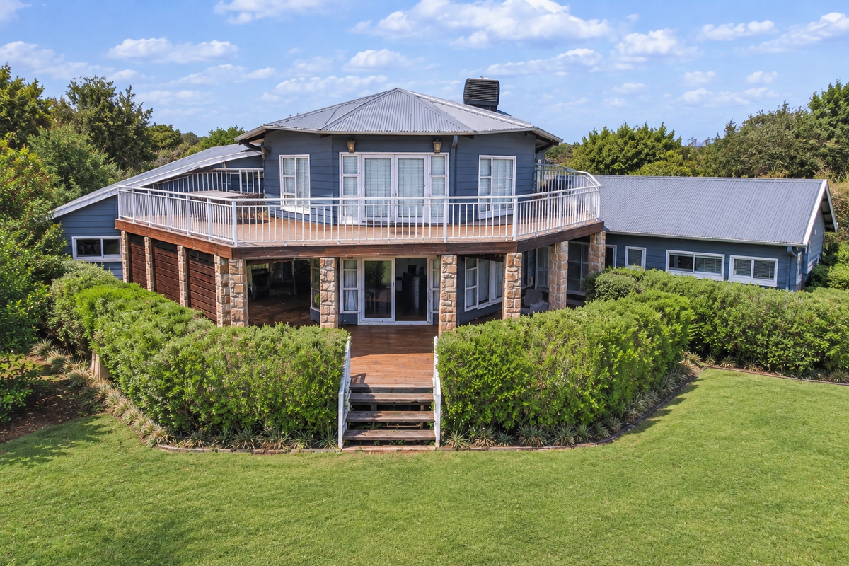 Rear view of a unique circular-design house featuring a large wrap-around balcony, timber decking, and stone-clad pillars overlooking a spacious garden.