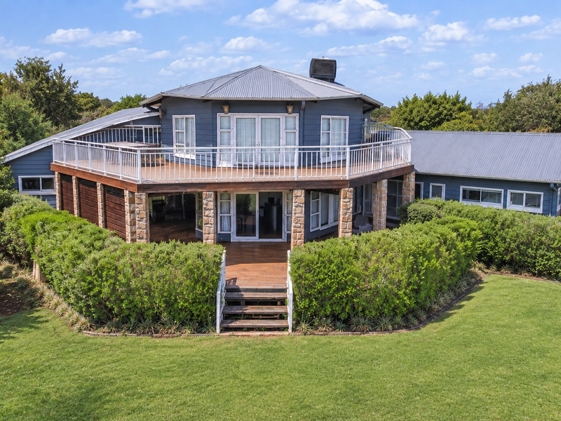 Rear view of a unique circular-design house featuring a large wrap-around balcony, timber decking, and stone-clad pillars overlooking a spacious garden.