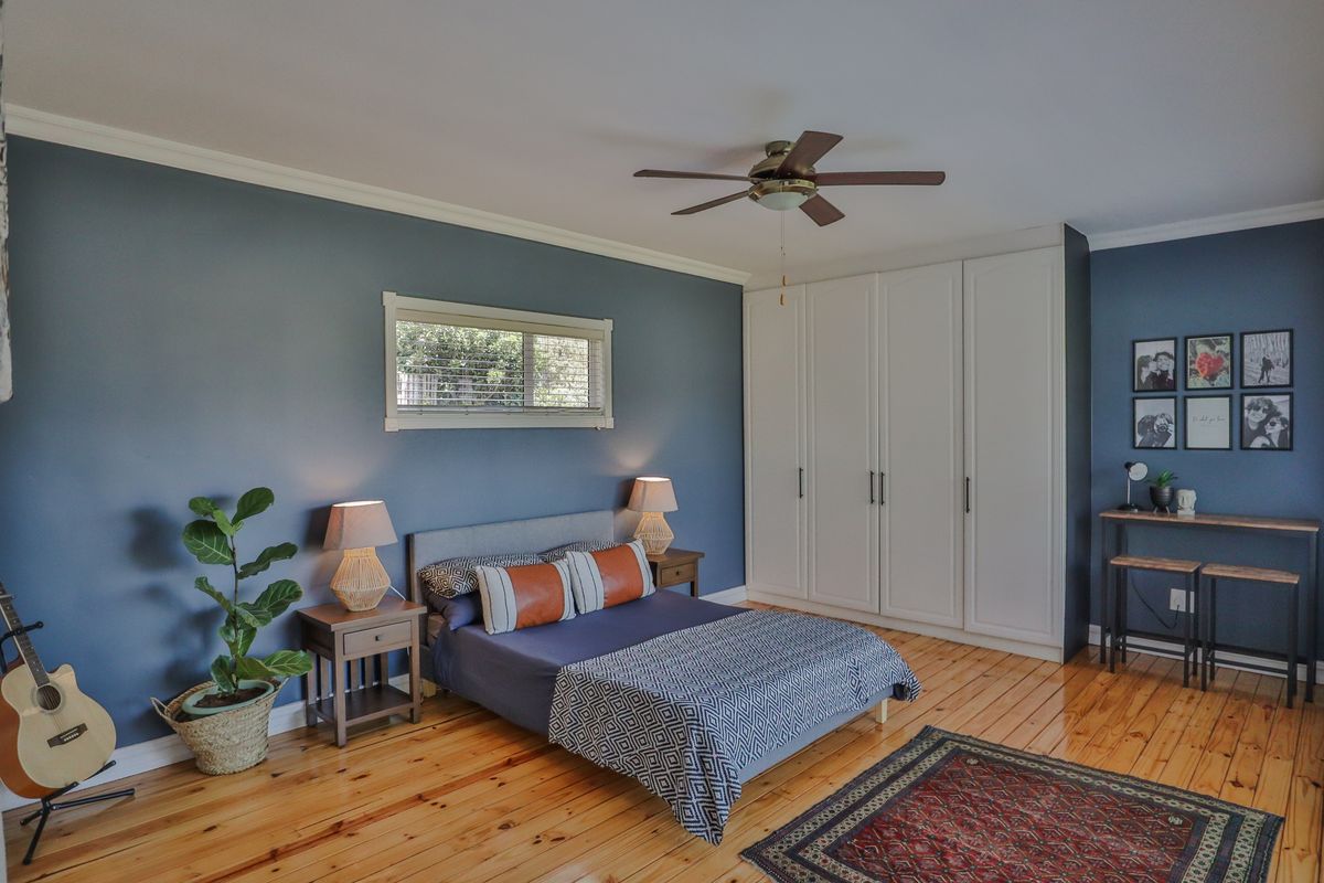 A well-maintained bedroom featuring polished timber flooring, a built-in wardrobe, and a ceiling fan, finished with blue accent walls.