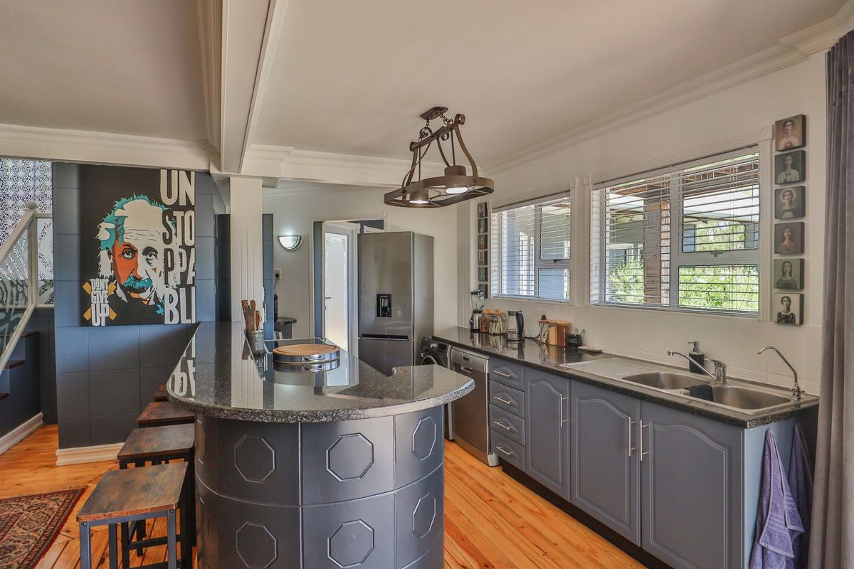 A well-lit kitchen featuring dark grey cabinetry, granite countertops, a breakfast bar, and natural hardwood flooring with large windows providing ample natural light.