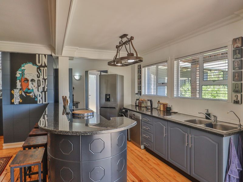 A well-lit kitchen featuring dark grey cabinetry, granite countertops, a breakfast bar, and natural hardwood flooring with large windows providing ample natural light.