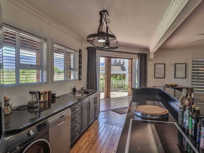 Modern kitchen featuring dark cabinetry, granite countertops, integrated appliances, and timber flooring, with direct access to an outdoor patio area.