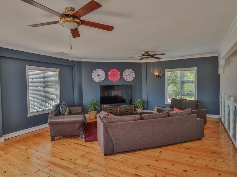 Spacious living room featuring polished hardwood flooring, crown molding, and dual ceiling fans, offering a comfortable and well-lit area for relaxation.
