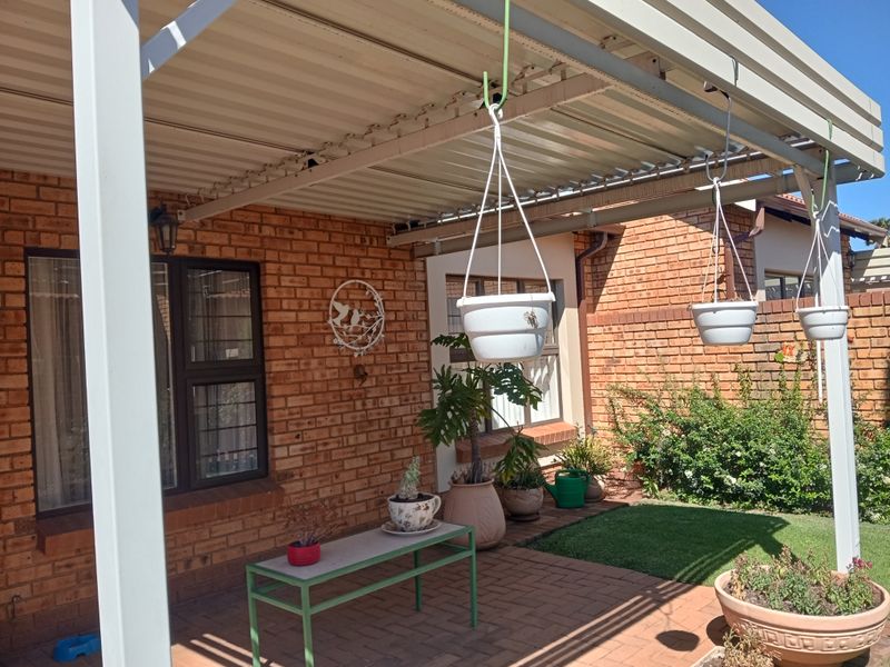 A covered brick patio area featuring a paved floor, corrugated metal roofing, and security-fitted windows, providing a pleasant outdoor space.