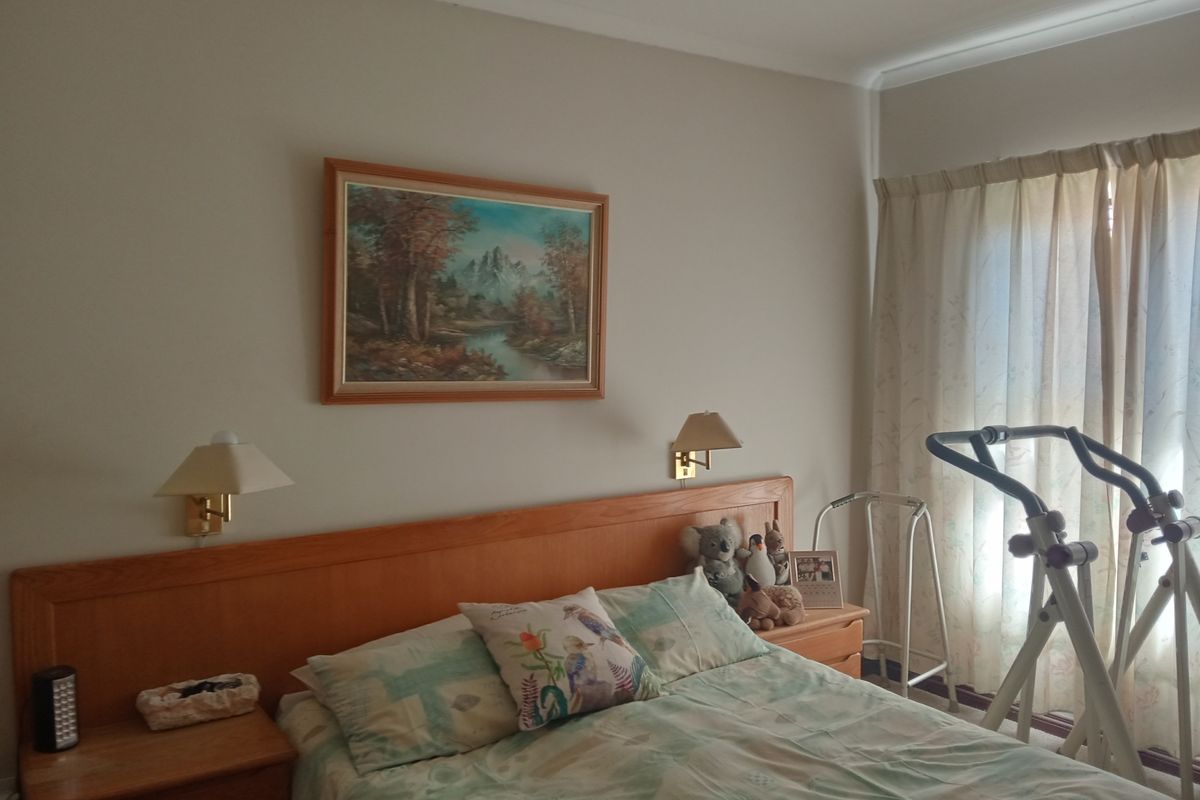 A comfortable bedroom featuring a built-in wooden headboard with integrated bedside lighting and large windows with curtains.