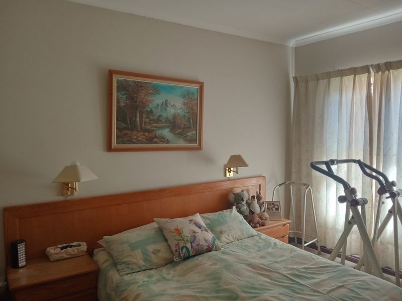 A comfortable bedroom featuring a built-in wooden headboard with integrated bedside lighting and large windows with curtains.