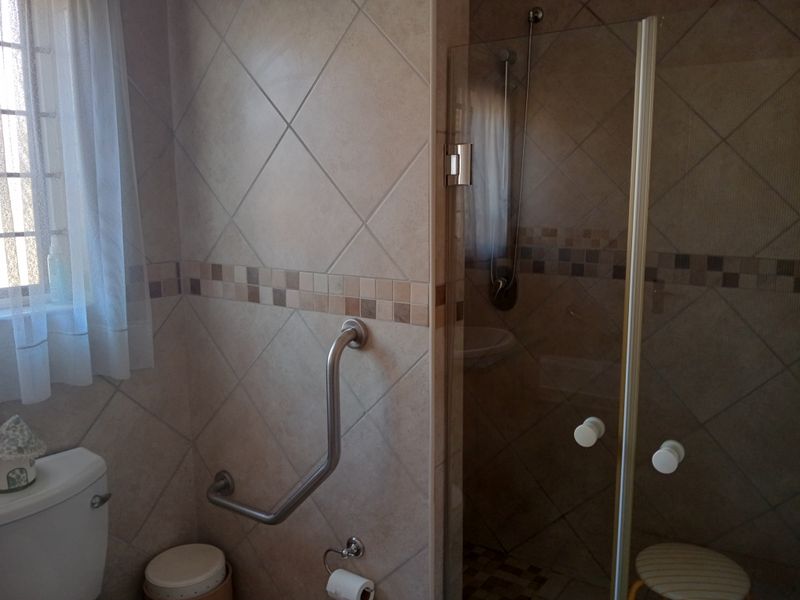 A functional bathroom featuring a tiled shower enclosure, toilet, and safety grab rail, suitable for retirement living requirements.