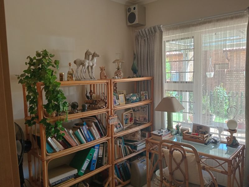 A functional home office space featuring a large window with natural light, neutral wall finishes, and a wall-mounted speaker.
