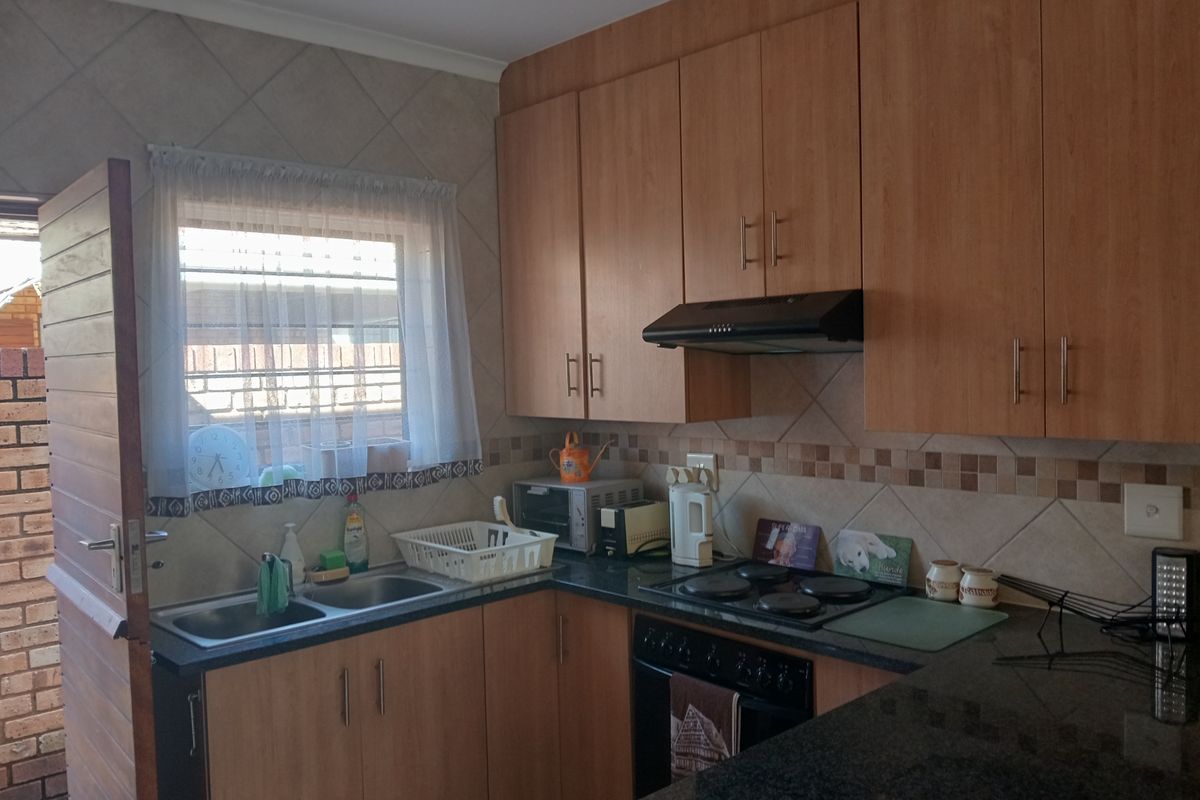 Functional kitchen featuring laminate cabinetry, granite countertops, built-in oven and hob, and a tiled backsplash with direct access to the exterior.