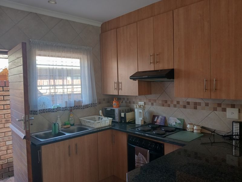 Functional kitchen featuring laminate cabinetry, granite countertops, built-in oven and hob, and a tiled backsplash with direct access to the exterior.