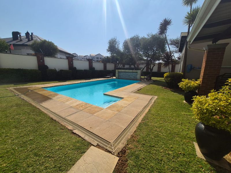 A well-maintained outdoor swimming pool area featuring stone coping, a built-in water feature, and a landscaped garden with perimeter walling.