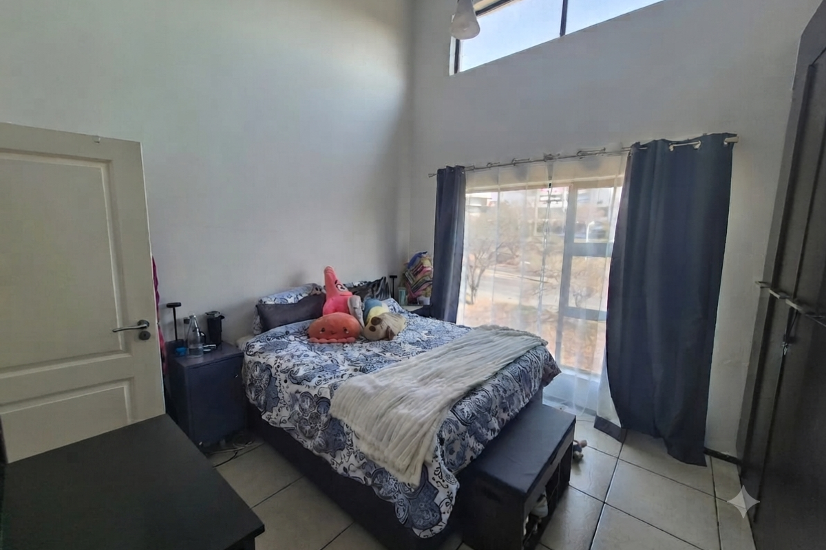 A bedroom featuring high ceilings, a large window with natural light, tiled flooring, and a built-in wardrobe.