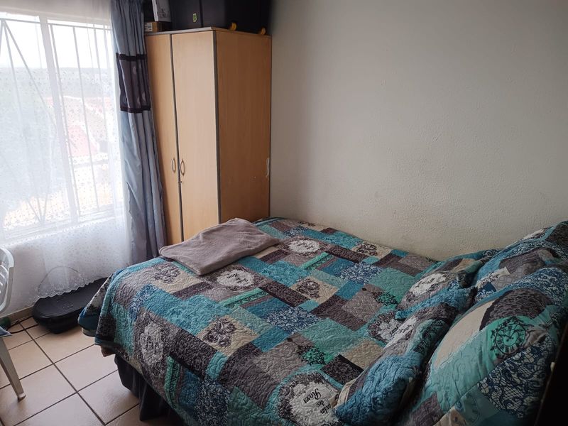 A functional bedroom featuring tiled flooring and a window fitted with security bars, providing natural light.