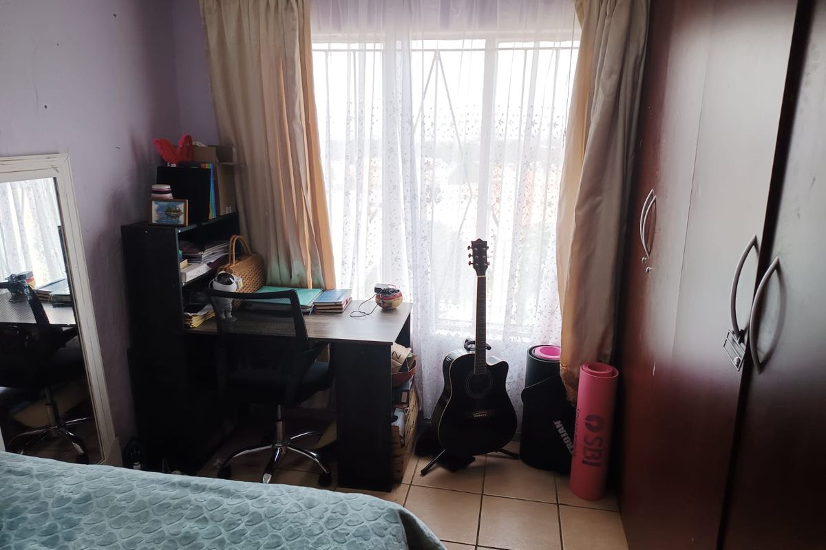 A bedroom featuring tiled flooring, a built-in wardrobe, and a window fitted with security bars.