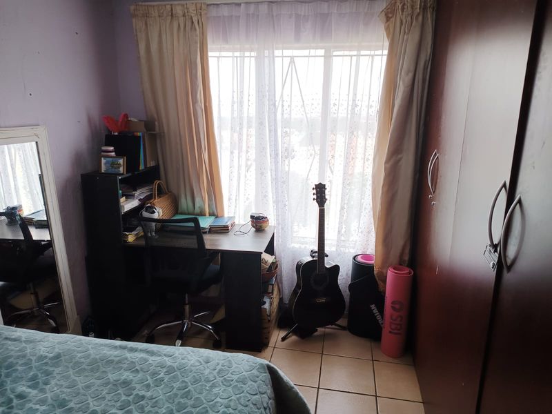 A bedroom featuring tiled flooring, a built-in wardrobe, and a window fitted with security bars.