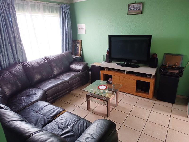A comfortable living room featuring tiled flooring and large windows with curtains, providing a functional space for relaxation.