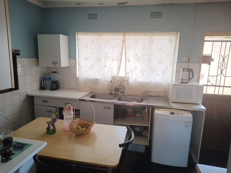 A functional kitchen area featuring a double stainless steel sink, tiled splashback, and built-in cabinetry, requiring some ceiling maintenance.