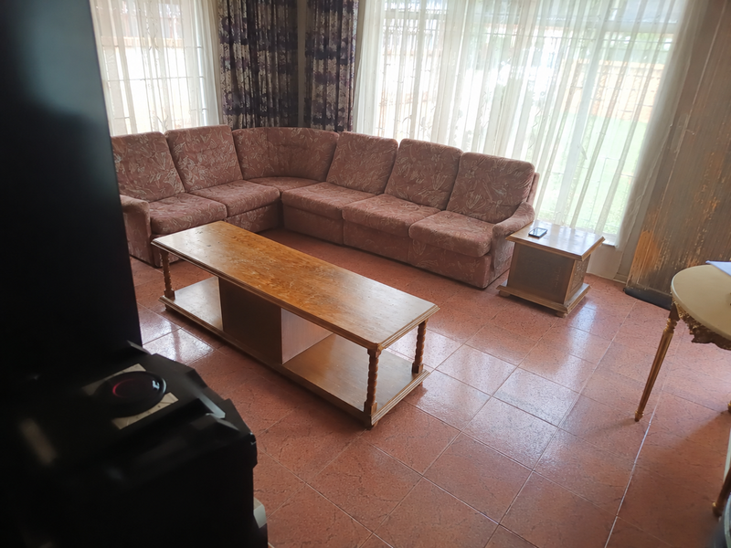 A living room featuring tiled flooring and large windows with curtains, offering a functional space with potential for modern updates.