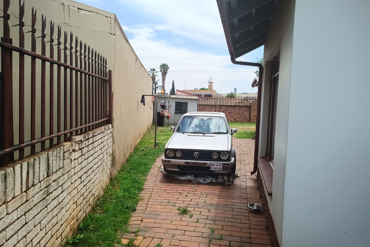 A narrow side yard featuring brick paving, a boundary wall with security spikes, and a roof overhang.