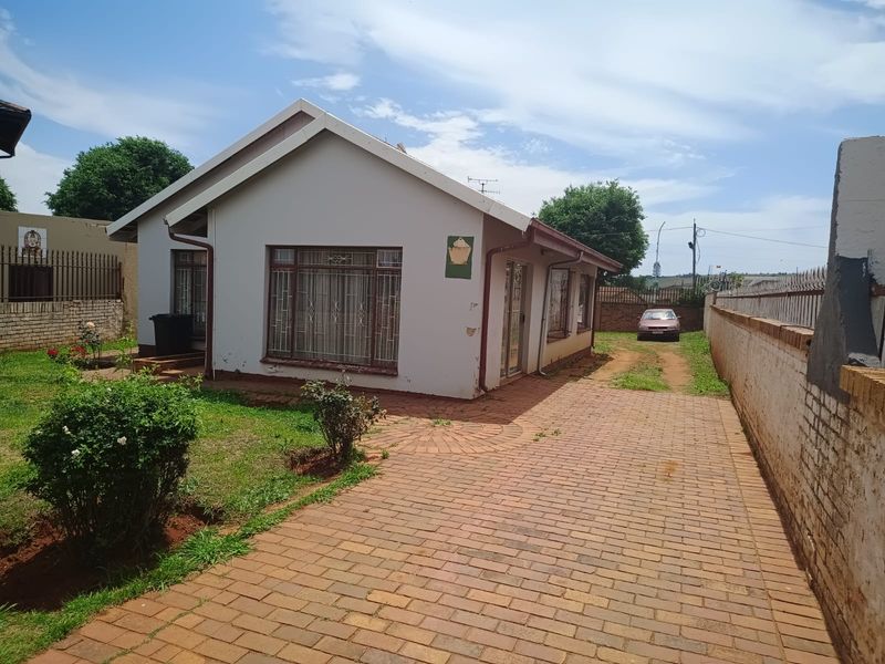 Front view of a detached house featuring a paved driveway, gabled roof architecture, and secure boundary walling.