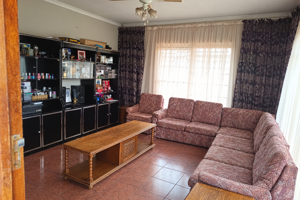 A living room featuring tiled flooring, a ceiling fan, and a large built-in shelving unit, offering a functional space with potential for modernization.