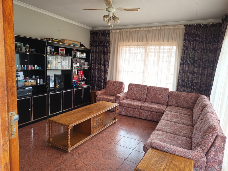 A living room featuring tiled flooring, a ceiling fan, and a large built-in shelving unit, offering a functional space with potential for modernization.