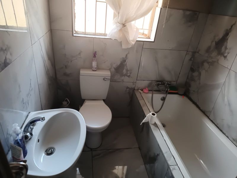 A compact bathroom featuring marble-effect wall and floor tiles, a pedestal basin, a standard toilet, and a built-in bathtub with a shower mixer.
